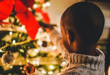 A little boy is reaching towards an out of focus Christmas tree.