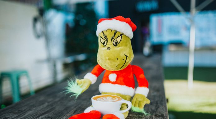 A stuffed Grinch plush sits on a bench with a latte in its lap.