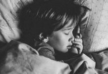 A black and white photo of a child sleeping in their bed.
