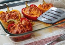 A glass casserole dish with five stuffed bell peppers and a spatula.
