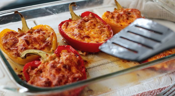 A glass casserole dish with five stuffed bell peppers and a spatula.